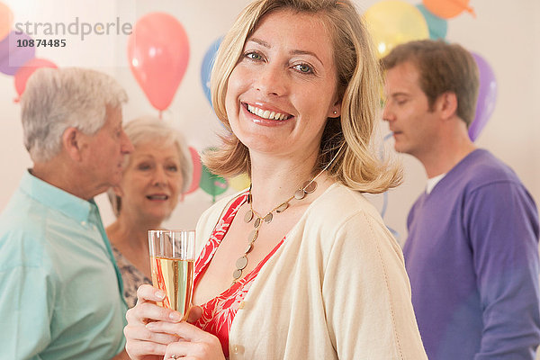 Frau auf der Party hält Champagnerflöte in der Hand und schaut lächelnd in die Kamera