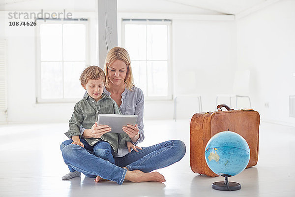 Reife Frau und Sohn sitzen auf dem Boden und schauen auf ein digitales Tablett