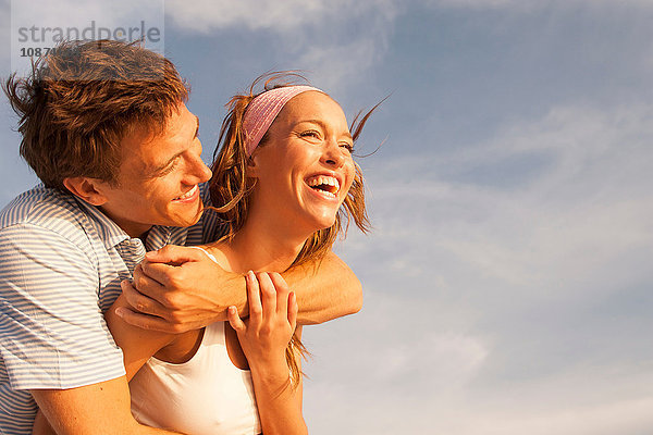 Mann umarmt Freundin vor blauem Himmel