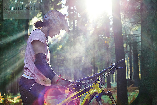 Mountainbikerin im Sonnenstrahl stehend mit gesenktem Kopf  Forest of Dean  Bristol  UK