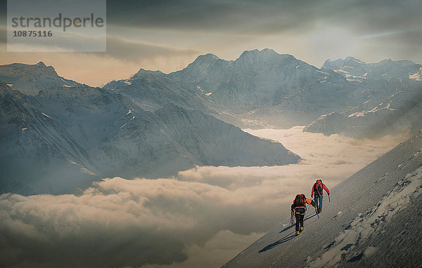 Zwei Bergsteiger auf einem verschneiten Hang über einem Nebelmeer in einem Alpental  Alpen  Kanton Wallis  Schweiz