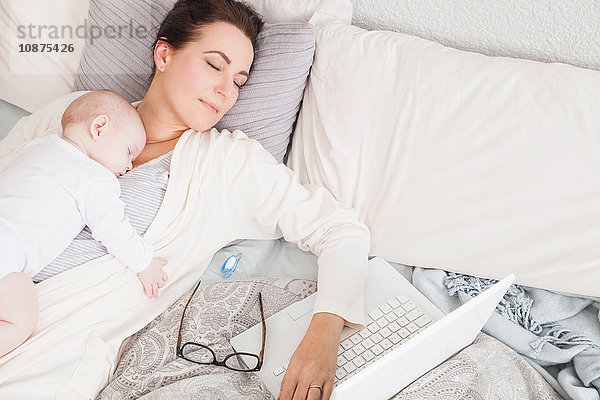 Mutter und Baby schlafen zusammen auf dem Bett  Laptop neben ihnen