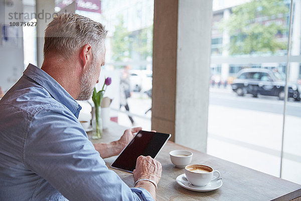 Älterer Mann sitzt im Café  benutzt digitales Tablett  Rückansicht