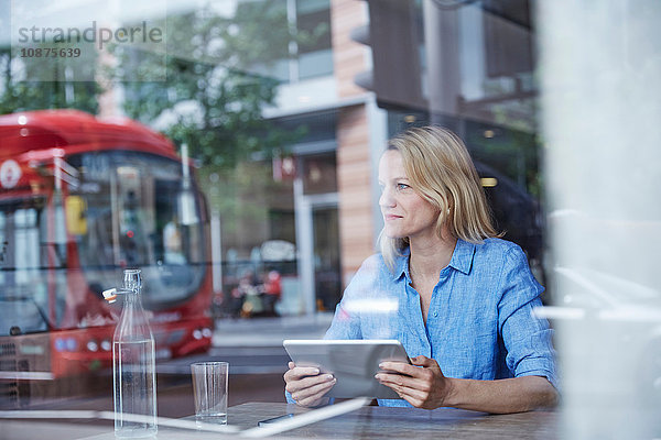 Reife Frau sitzt im Café  benutzt digitales Tablet  Bus spiegelt sich im Fenster