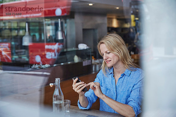 Reife Frau sitzt im Café  benutzt Smartphone  Bus spiegelt sich im Fenster