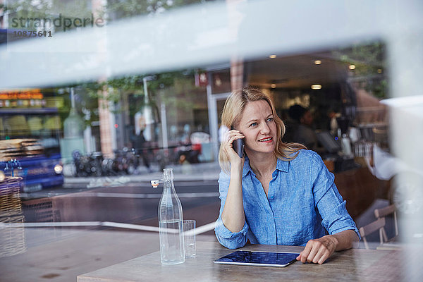 Reife Frau sitzt im Café und benutzt ein Smartphone