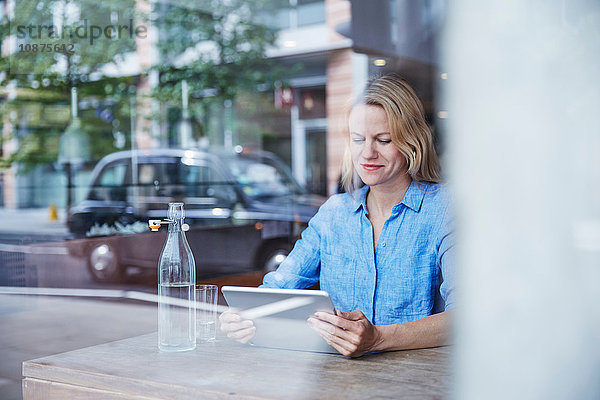 Reife Frau sitzt im Café  benutzt digitales Tablet  Taxi spiegelt sich im Fenster