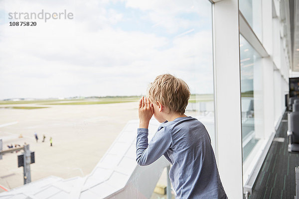 Junge schaut aus dem Flughafenfenster auf die Startbahn
