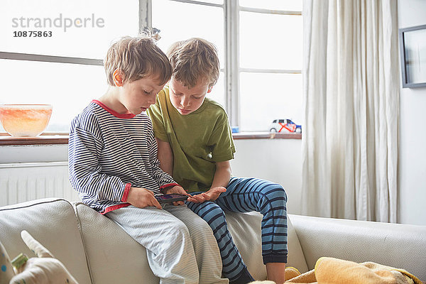 Jungen in Pyjamas sitzen auf dem Sofa und schauen auf Smartphone