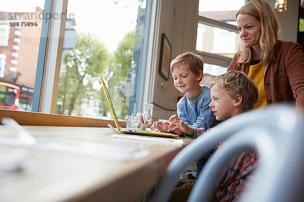 Mutter und Sohn am Fensterplatz im Café mit Laptop