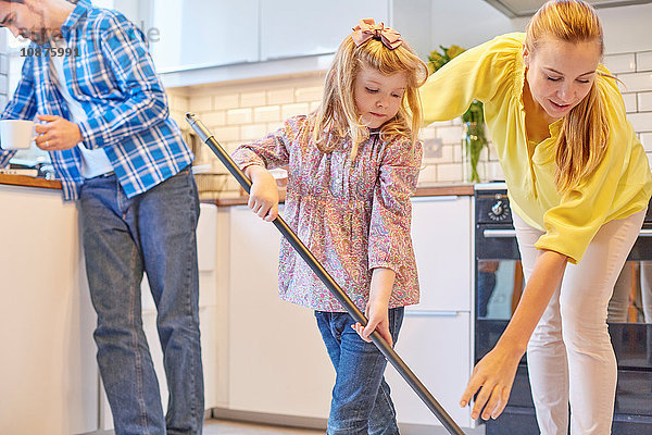 Mutter und Tochter wischen den Küchenboden  der Vater liest im Hintergrund