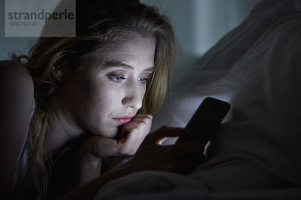 Nahaufnahme einer jungen Frau  die nachts im Bett liegt und Smartphone-Texte liest