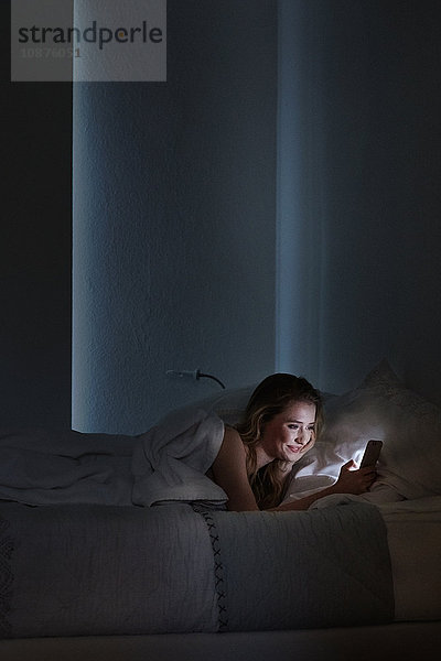 Junge Frau liegt nachts im Bett und liest Smartphone-Texte