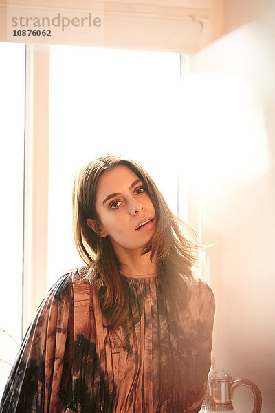 Porträt einer jungen Frau vor einem sonnenbeschienenen Fenster