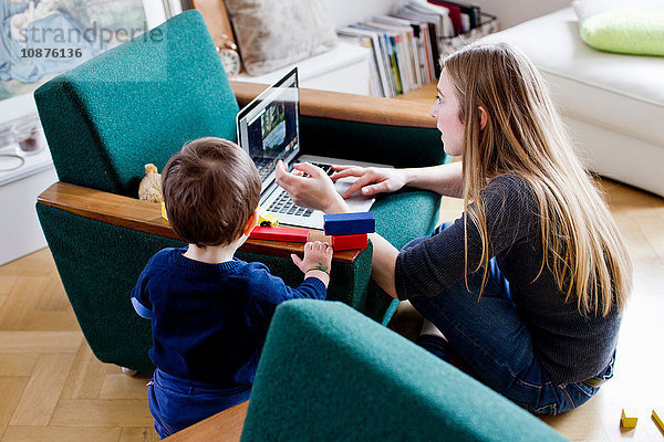 Mittelgroße erwachsene Frau und kleiner Sohn schauen auf den Laptop im Wohnzimmer