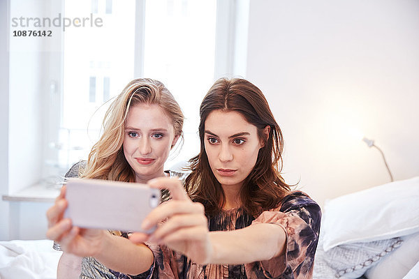 Zwei junge Frauen sitzen im Bett und nehmen Smartphone-Selfie