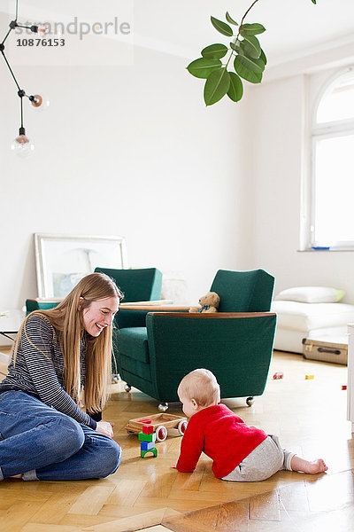 Mittelgroße erwachsene Frau und kleine Tochter spielen mit Bauklötzen auf dem Wohnzimmerboden