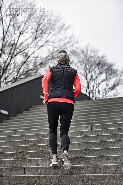 Rückansicht einer reifen Läuferin  die eine Stadttreppe hinaufläuft