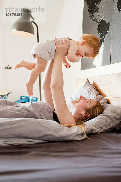 Mittlere erwachsene Frau  die ihre kleine Tochter im Bett hochhält