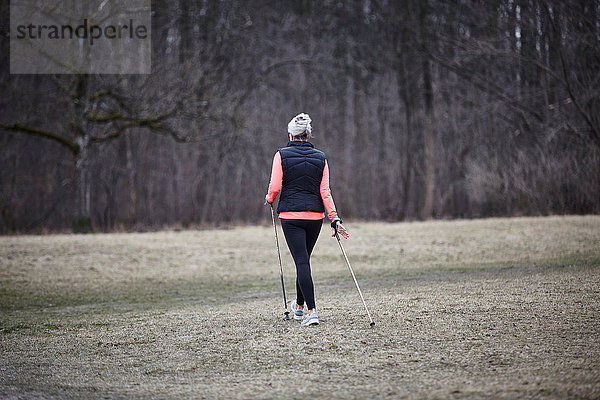 Rückansicht eines reifen Frauentrainings im Park  Nordic Walking mit Stöcken