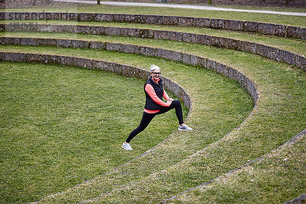 Reife Frau trainiert im Park  streckt die Beine auf der Rasentreppe