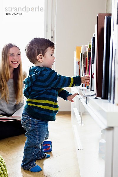 Mittlere erwachsene Frau  die zuschaut  wie ihr kleiner Sohn die ersten Schritte macht