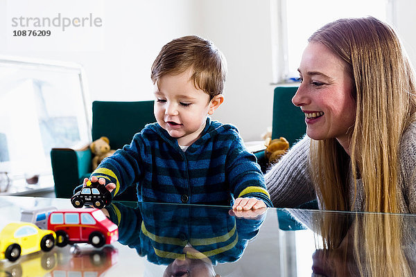 Mittlere erwachsene Frau und kleiner Sohn spielen mit Spielzeugautos auf dem Tisch