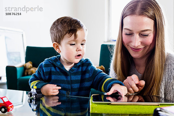 Mittelgroße erwachsene Frau und kleiner Sohn verwenden Touchscreen auf digitalem Tablett am Tisch