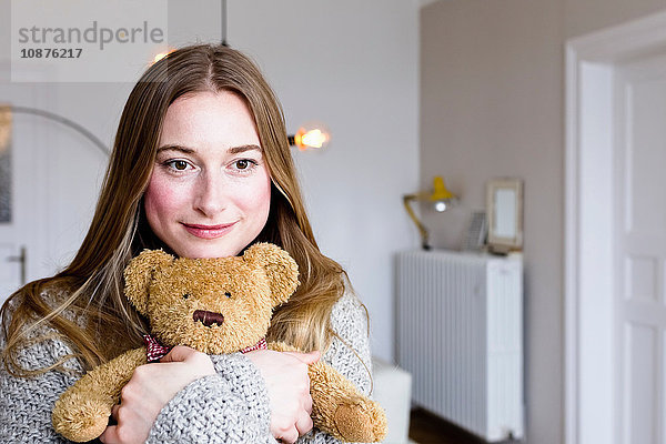 Porträt einer mittleren erwachsenen Frau im Wohnzimmer  die einen Teddybär umarmt