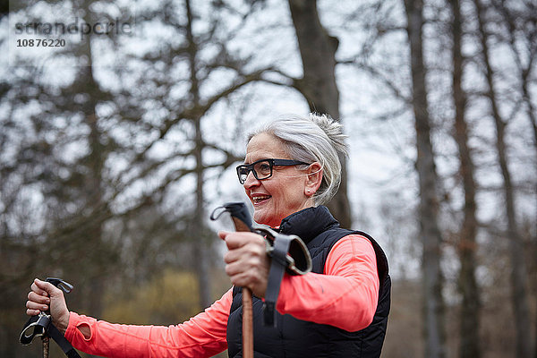 Reife Frau trainiert im Park  stehend mit Nordic-Walking-Stöcken