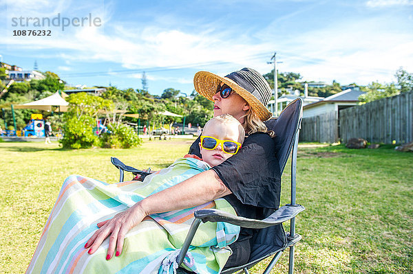 Junge mit gelber Sonnenbrille sitzt auf dem Schoß der Mutter im Park  Waiheke Island  Neuseeland