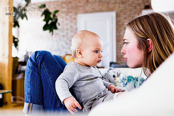 Mittelgroße erwachsene Frau und kleine Tochter ziehen sich auf dem Sofa das Gesicht