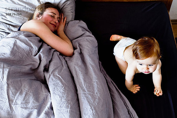 Kleines Mädchen krabbelt auf dem Bett  während sich die Mutter entspannt