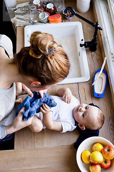 Draufsicht einer Frau  die ihr Baby Sohn für ein Bad in der Küchenspüle entkleidet