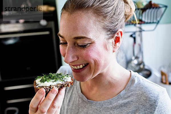 Mittlere erwachsene Frau isst Roggenbrot-Snack in der Küche