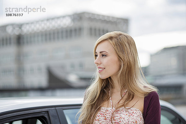 Langhaarige blonde junge Frau wartet mit dem Auto in der Stadt