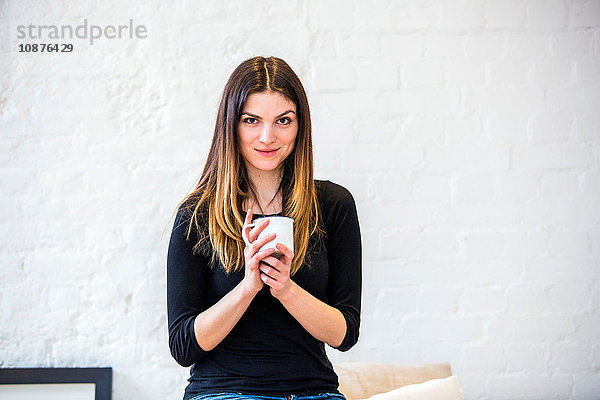 Porträt einer schönen jungen Frau in Wohnung mit Kaffeebecher