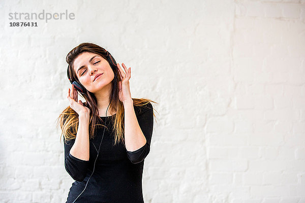 Hübsche junge Frau wiegt sich zu Kopfhörermusik vor weißer Wand