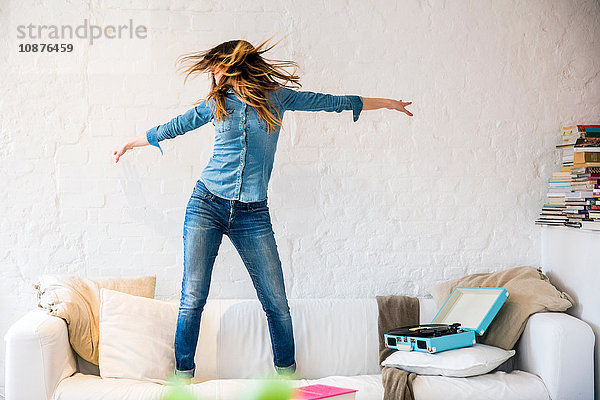 Junge Frau steht auf dem Sofa  tanzt und schüttelt ihr Haar