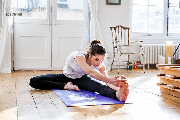 Junge Frau praktiziert Yoga  berührt Zehen in Wohnung