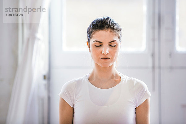 Junge Frau meditiert mit geschlossenen Augen in Wohnung