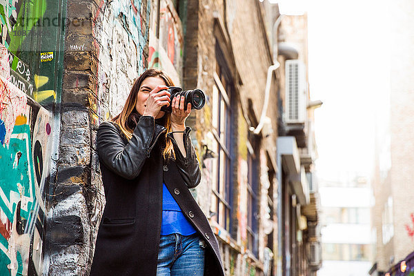 Junge Frau fotografiert in Graffiti-Gasse mit DSLR