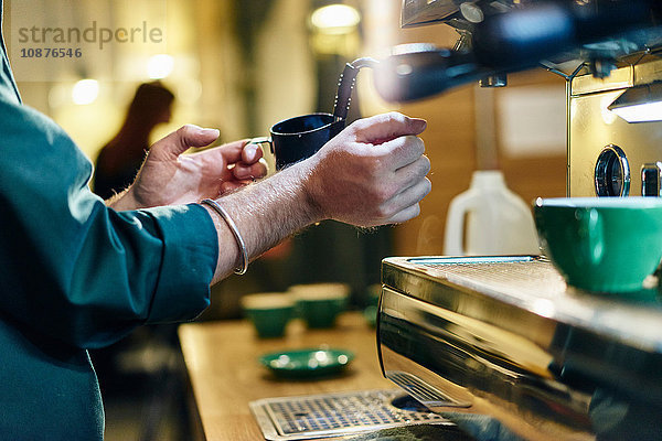 Schnappschuss eines männlichen Barista beim Erhitzen des Milchkännchens auf der Kaffeemaschine im Café