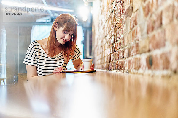 Weibliche Kundin sitzt auf Bank und blättert auf digitalem Tablet im Café