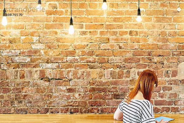 Weibliche Kundin sitzt an Backsteinwandbank und blättert auf digitalem Tablet im Café