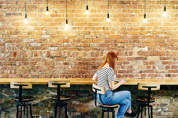 Weibliche Kundin sitzt an Backsteinwandbank und blättert auf digitalem Tablet im Café