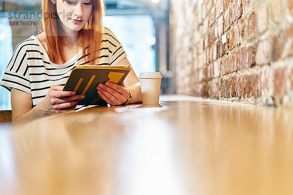 Junge Frau sitzt auf Bank und blättert auf digitalem Tablet im Café