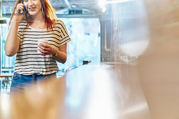 Junge Frau im Coffeeshop mit Kaffee zum Mitnehmen plaudert auf dem Smartphone