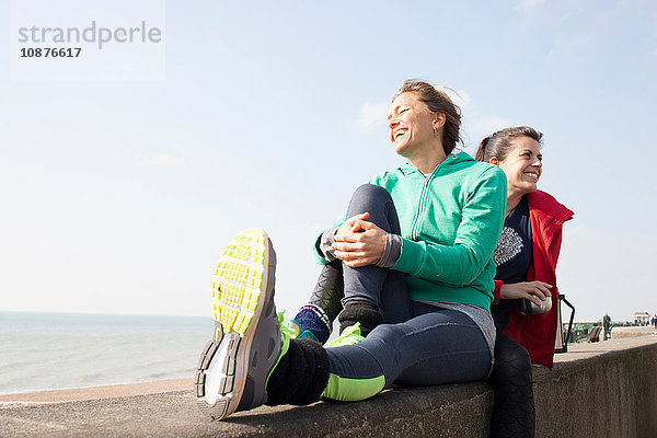 Zwei Läuferinnen machen eine Kaffeepause an der Wand am Strand von Brighton