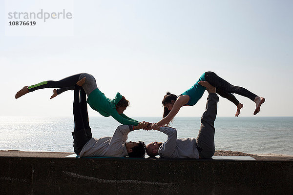 Silhouettierte Männer und Frauen praktizieren akrobatisches Yoga an der Wand am Strand von Brighton